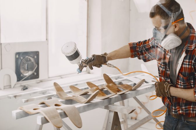 Yooung repairman carpenter working with paint painting. Master painter in a factory painting wood with spray gun.